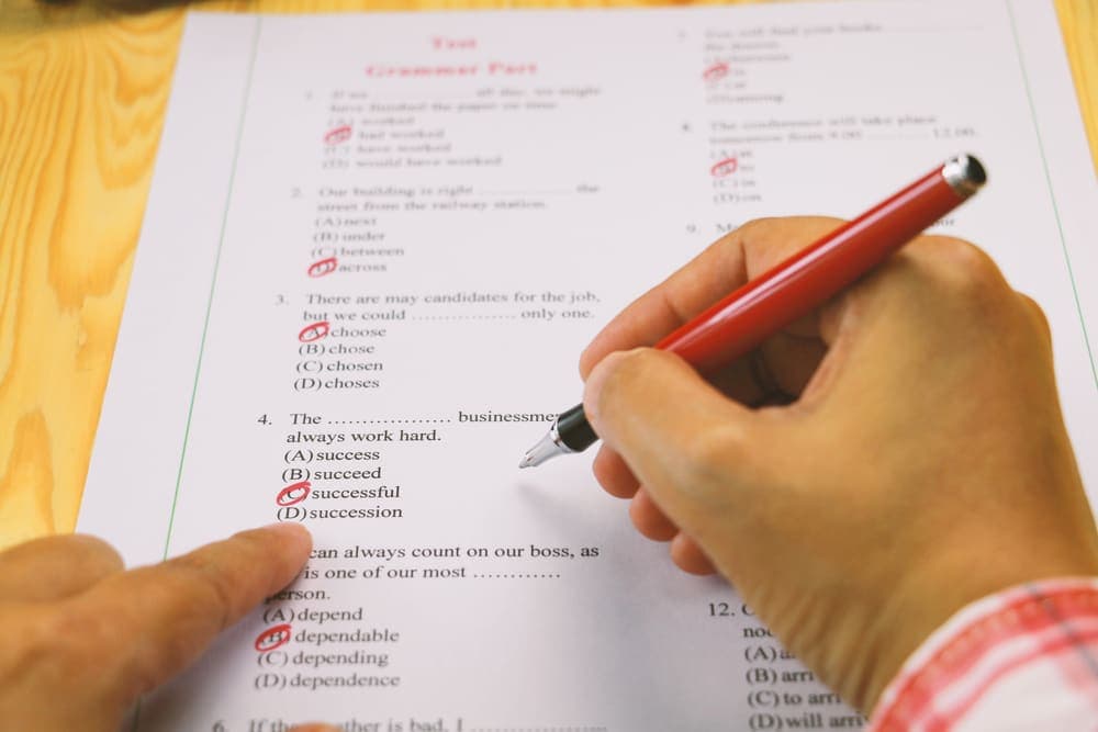 A student marking multiple-choice answers with a red pen on a past paper
