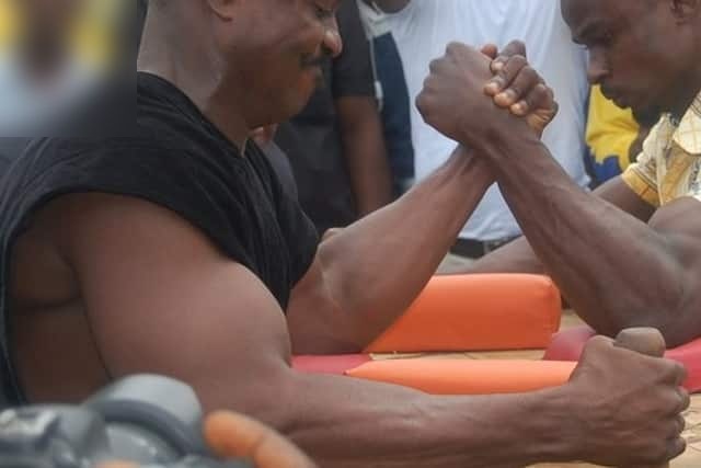 Two men arm wrestling across a table, their bent arms locked and upper-arm muscles bulging.