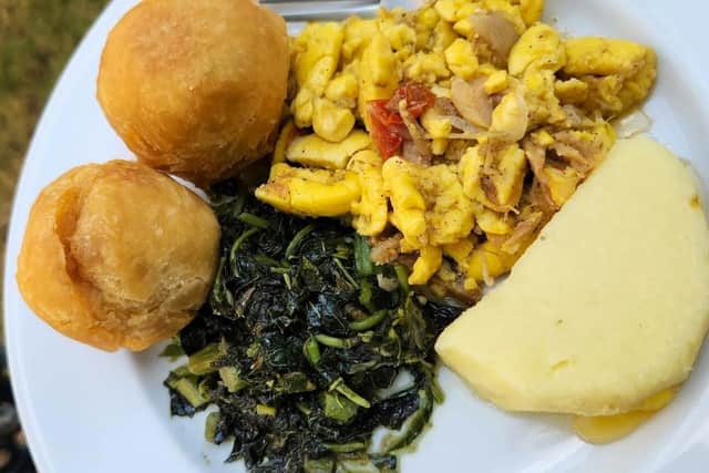 A Jamaican breakfast on a white plate: ackee and saltfish, dark green callaloo, two fried dumplings and a slice of boiled yam.
