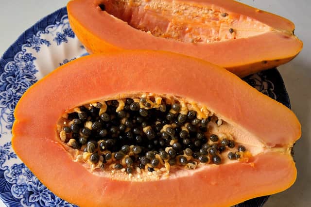 A ripe papaya cut in half on a blue and white plate, showing orange flesh and black seeds.
