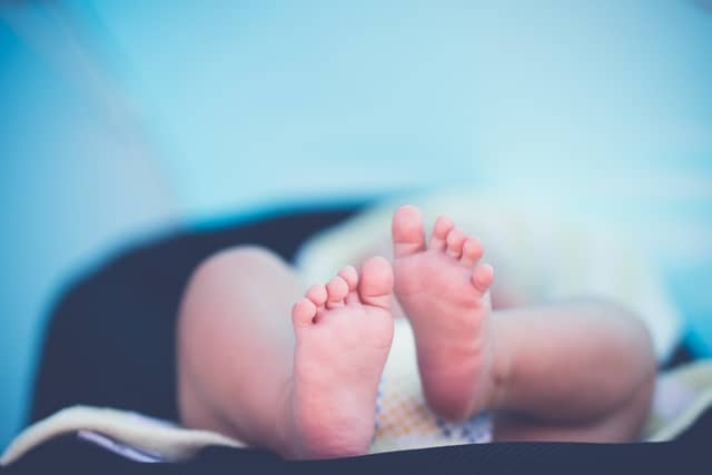 The tiny bare feet of a newborn baby, lying on a soft blanket.