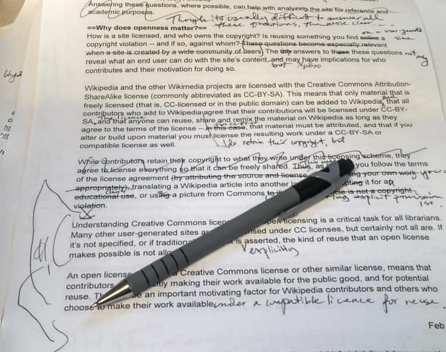 A printed page covered in handwritten corrections: words crossed out, others written in, and a pen lying on top.
