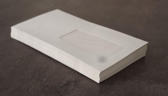 A thick stack of white window envelopes on a dark table.