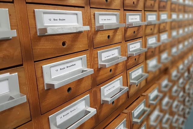A long wall of wooden filing drawers, each with a metal label holder showing the range of names inside.