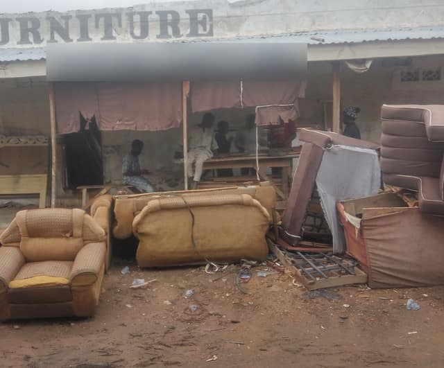 A roadside furniture workshop with a FURNITURE sign: armchairs and sofas wait outside while workers build more inside.
