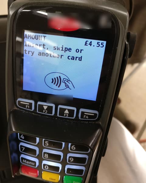 A hand-held card machine whose screen shows an amount of 4.55 and the words insert, swipe or try another card, above a tap-to-pay symbol and a keypad.