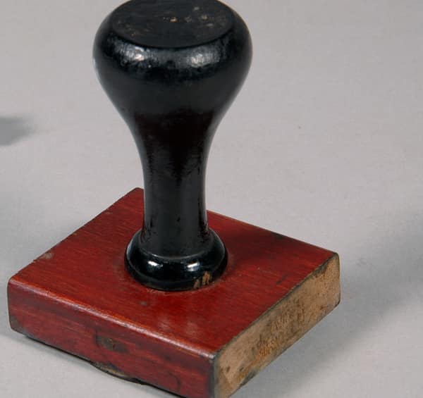 An old office rubber stamp with a black wooden handle and a red base.