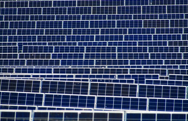 Row after row of solar panels angled towards the sun across a large solar farm.