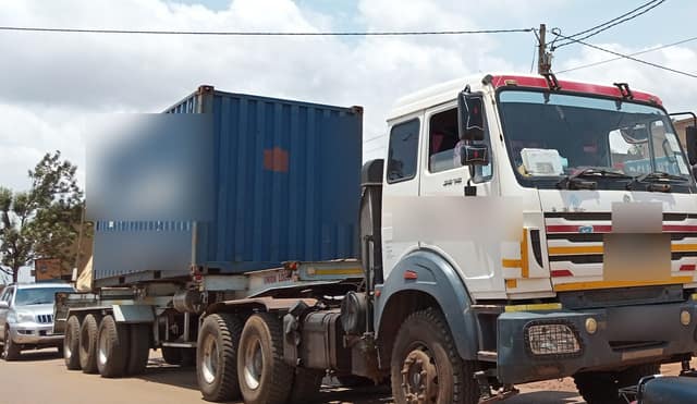 A white lorry pulling a blue shipping container on a trailer along a town street.